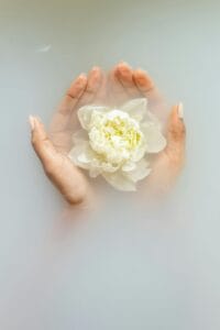 mains dans l'eau blanche laiteuse tenant une fleur blanche à la surface
